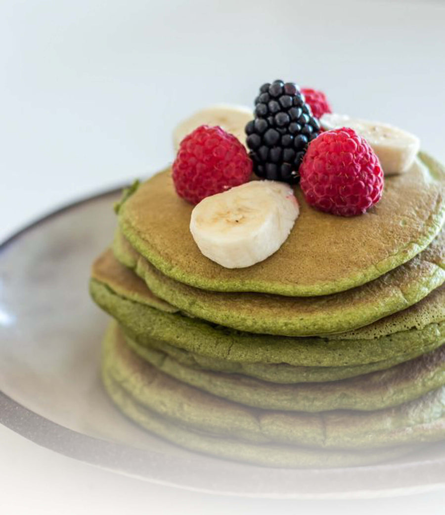 Stapel groene matcha pancakes met ahornsiroop en verse aardbeien