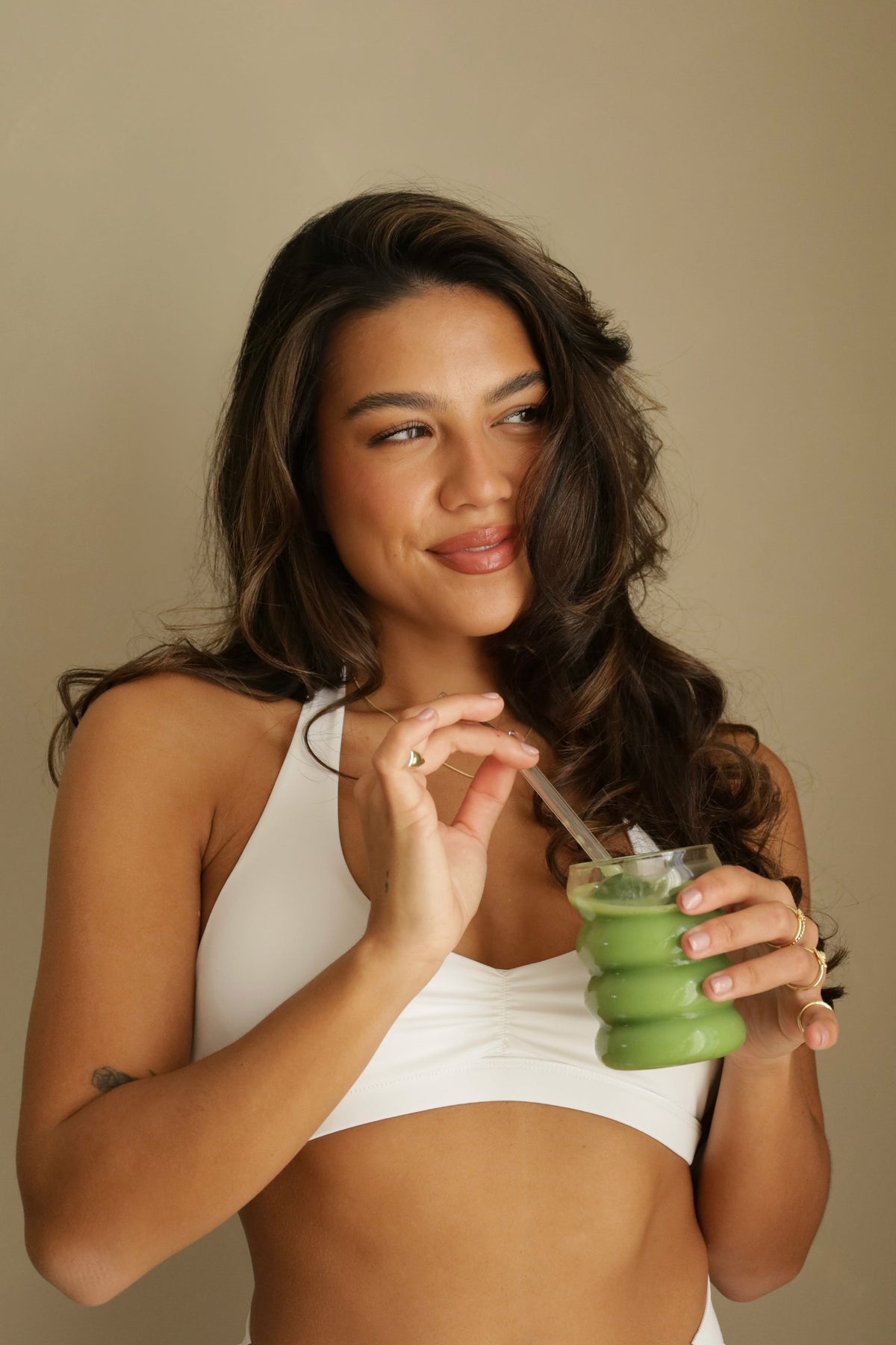 Vrouw in wit sporttopje drinkt iced matcha uit een groen glas met glazen rietje