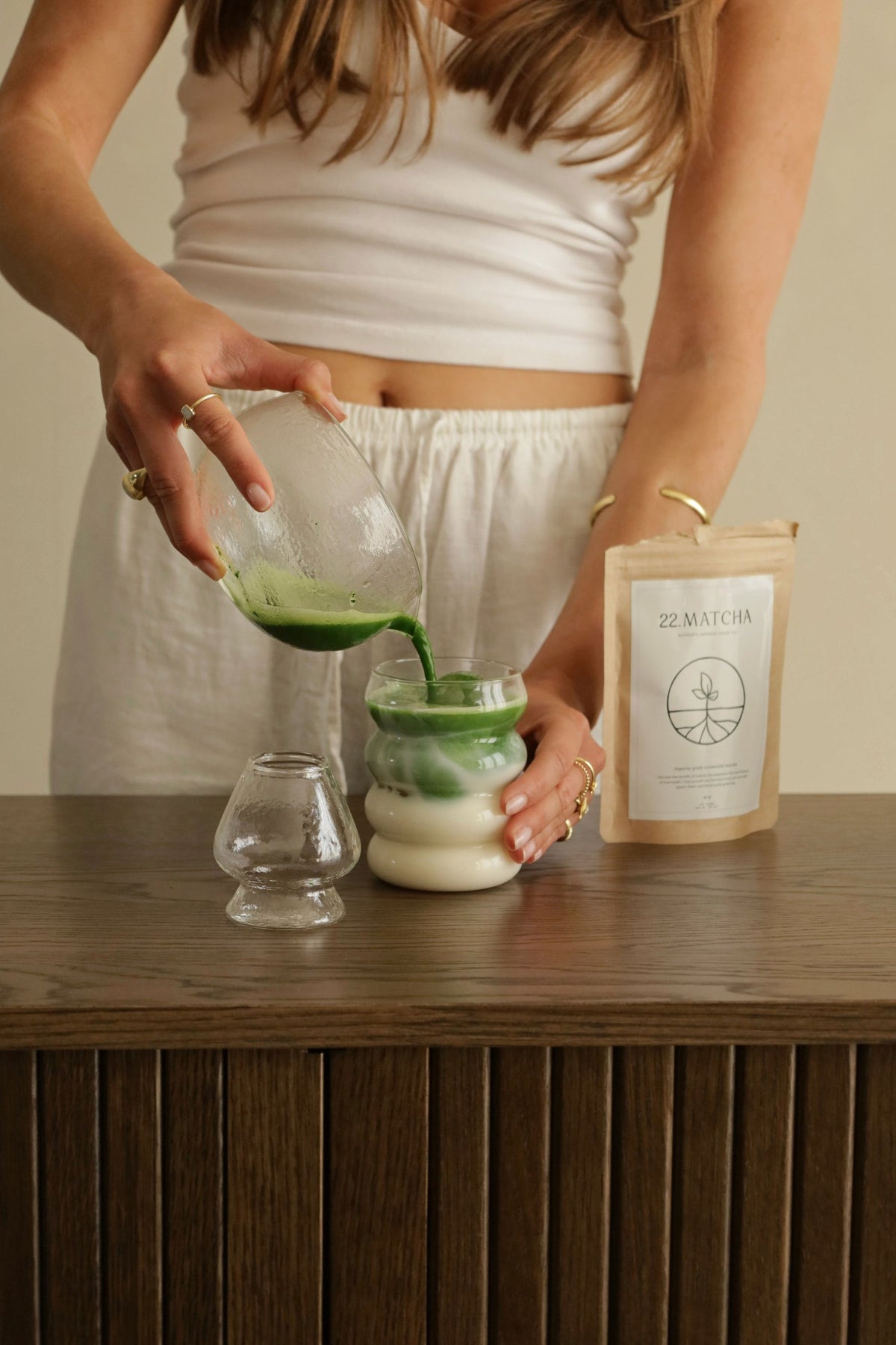 Matcha wordt uit een glazen kom in een glas met melk geschonken, naast het 22.Matcha zakje