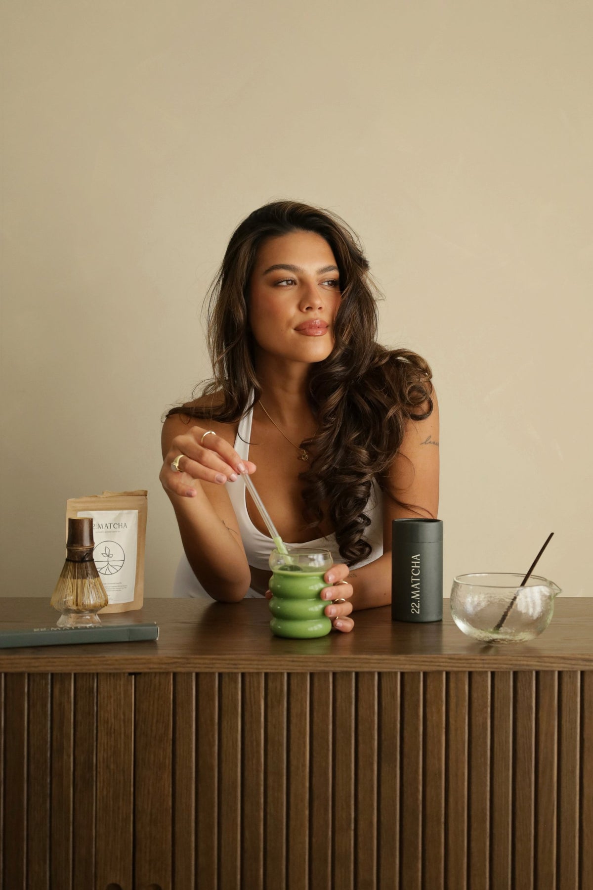 Vrouw roert matcha aan een houten dressoir, met het 22.Matcha zakje, bamboe klopper en voorraadblik.